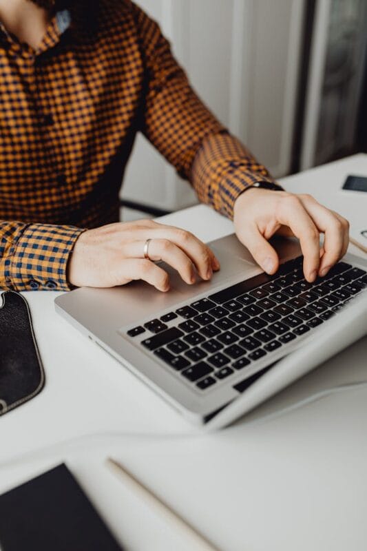 A man typing on a laptop in a modern office setting, showcasing technology and work life.
