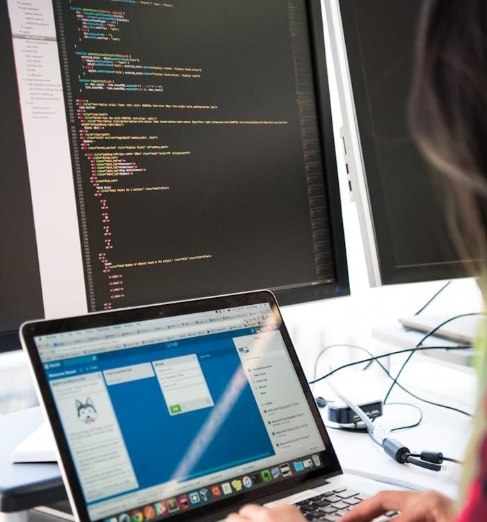 Programmer working on code across multiple screens in a modern office setting.