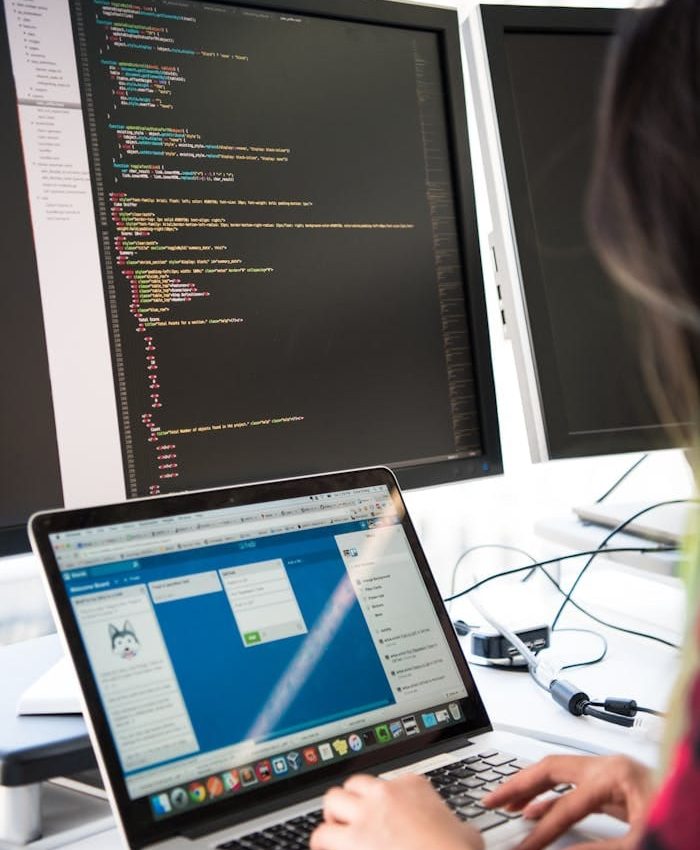 Programmer working on code across multiple screens in a modern office setting.
