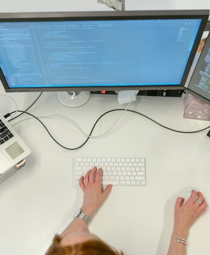 A female software engineer coding on dual monitors and a laptop in an office setting.