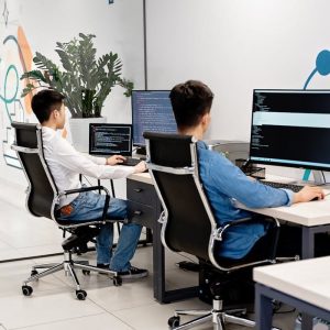 Two programmers collaborating in a bright, modern office, coding on monitors.